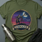 Backyard Astronomer (F) sci-fi t-shirt — a vintage figure at a tripod telescope under a starry sky with a sunset-stripes sun behind — Military Green unisex tee — Apsion Outpost