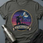 Backyard Astronomer (M) sci-fi t-shirt — a vintage figure at a tripod telescope under a starry sky with a sunset-stripes sun behind — Dark Heather unisex tee — Apsion Outpost